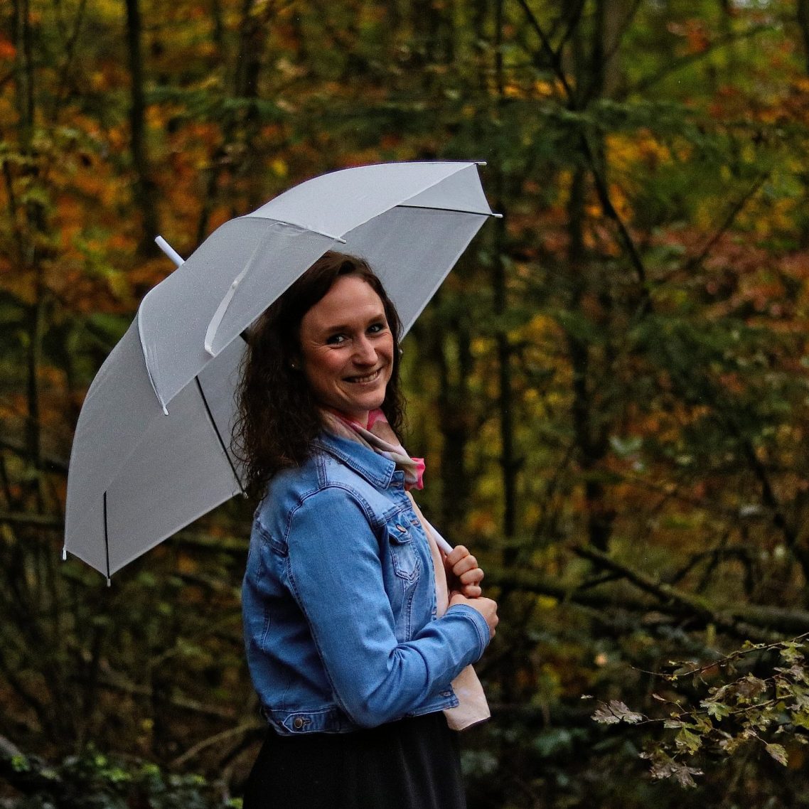 Über mich... Frau mit Regenschirm steht in einem herbstlichen Wald.