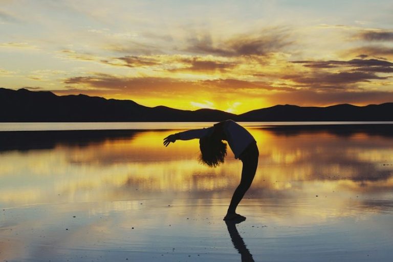 Yoga am Abend Person in einer Yoga-Positur vor einem Sonnenuntergang in einem See stehend.